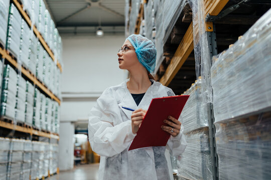 Female worker in protective workwear working in medical supplies research and production factory and checking packed canisters of distilled water before shipment. Industrial warehouse.