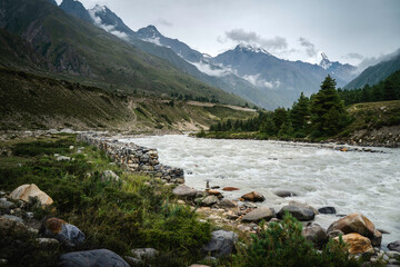 Fototapeta na wymiar View of Baspa river flanked by boulders and Himalayas under overcast sky. Chitkul, India. 