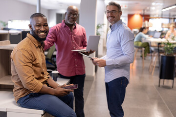 Obraz premium Portrait of smiling multiracial male business colleagues with wireless technologies at modern office