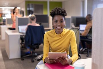 Portrait of smiling african american young businesswoman sitting with digital tablet at office - obrazy, fototapety, plakaty