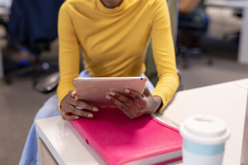 Midsection of young african american businesswoman holding digital tablet at workplace