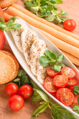 Vertical image of traditional italian caprese salad with baby tomatoes and sliced mozzarella, basil, olive oil, corn salad, bruschettas and grissini on wooden table background. Classic appetizer