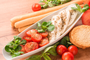 Traditional italian caprese salad with baby tomatoes and sliced mozzarella, basil, olive oil, corn salad, bruschettas and grissini on wooden table background. Classic restaurant appetizer