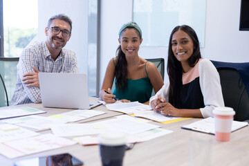 Portrait of happy multiracial businessman and businesswomen sitting in boardroom during meeting