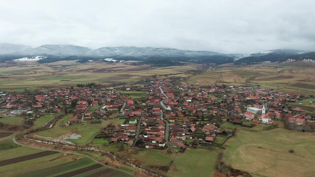 Flyover above homes, buildings of Sancraieni, Romania. Ciuc Mountains in background