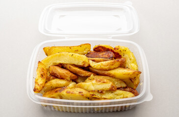 Baked potatoes wedges in transparent food-grade plastic box for refrigeration or storing, on light gray background