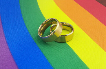 Two gold wedding rings on rainbow LGBT pride flag close-up. 