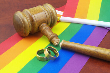 LGBT marriage equality and laws concept. Two wedding rings, broken wooden gavel and LGBT flags 	
