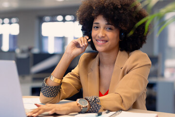 Portrait of happy african american female telecaller with headset using laptop at workplace