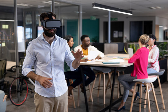 Caucasian businessman wearing vr headset against multiracial colleagues in meeting at workplace