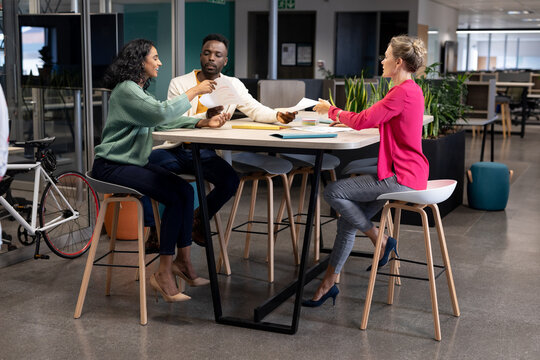 Multiracial business colleagues discussing over document during meeting at modern workplace