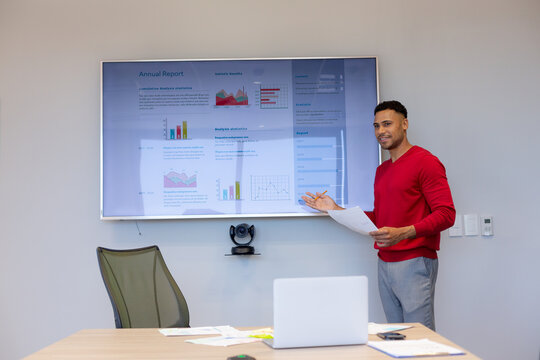 Hispanic Businessman Giving Presentation On Television Screen In Boardroom During Meeting At Office