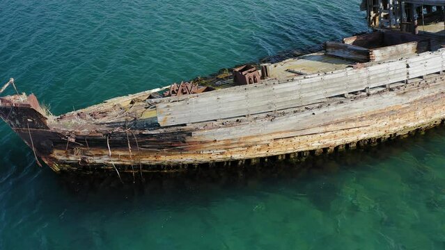 Abandoned wooden hunting schooner Lakhtak built in 1953 in Vityaz Bay. A wrecked wooden ship lies on the seashore, covered with rust. Drone view