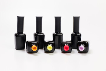 black bottles of varnishes stand in a row along with open bottles of multicolored varnish. bright varnishes of orange, yellow, pink and lilac colors lie open on a white background