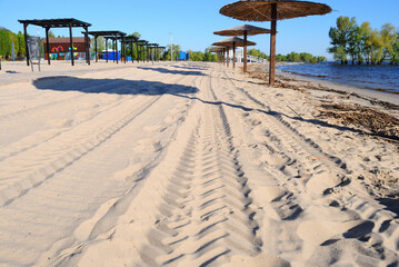 Calm and empty beach before the arrival of visitors. A fresh pattern of wheels on the sand.