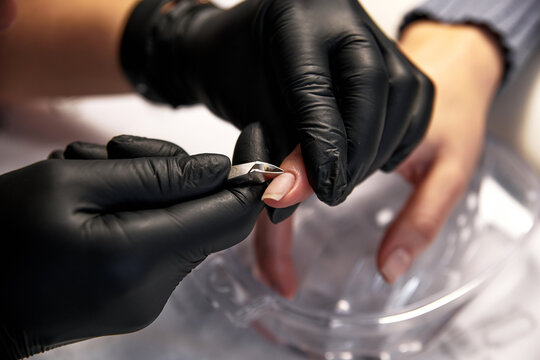 the master does a manicure to a woman with clean nails. a master in black latex gloves cuts off the cuticle on a woman's nails close-up with nail clippers