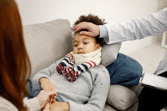 Male pediatrician holding hand on a forehead of sick little black girl