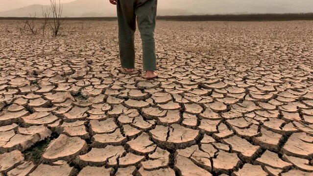A man walking barefoot on dry lake or river. Stepping on Cracked soil metaphor Climate Change and Drought impact or CO2 affect.