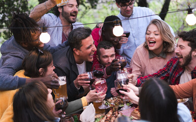 Cheerful friends having fun picnic while toasting with wine, beer and drinks - Friends like a family concept and enjoying life