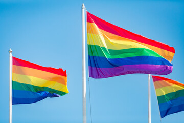 Rainbow flag fluttering against blue sky, Pride LGBT community symbol