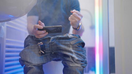 Bathroom with headless gamer in haze and RGB play video game on smartphone winning