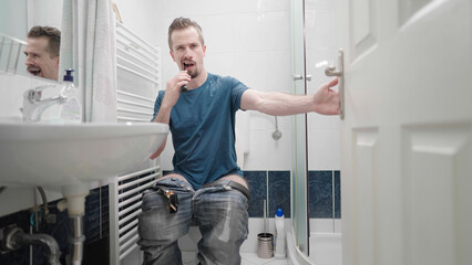 Fototapeta na wymiar Bathroom invasion of privacy with man on toilet washing teeth multitasking