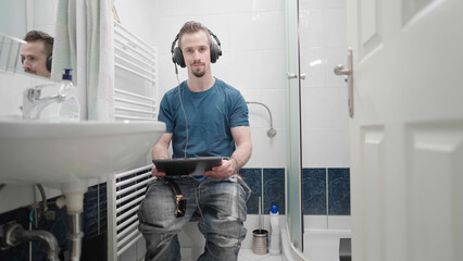 Fototapeta premium Bathroom with man watching movie on tablet with headphones
