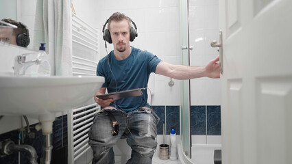 Bathroom with man watching movie on tablet with headphones closing door