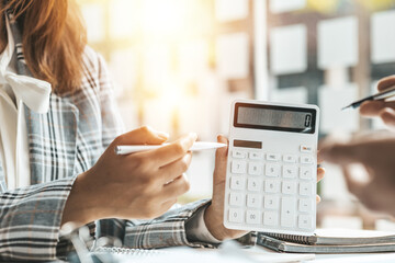 A person holding a white calculator, a group of businessmen in a meeting room discussing and verifying the account numbers in the company's financial statements for accuracy. Business meeting concept.