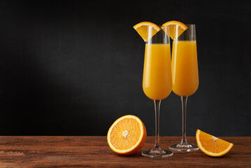 A pair of mimosa cocktail in flute glass with orange slice on a wooden bar and dark background.