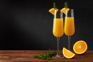 A pair of mimosa cocktail in flute glass with orange slice and rosemary twig on a wooden bar and...