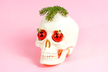 White skull with Xmas balls and fir tree on light pink background. Christmas and New Year celebration concept.