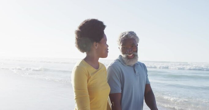 Happy african american couple walking and talking on sunny beach