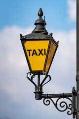 A taxi street lamp against a spring sky indicates where taxis should stop on a London, England, street.