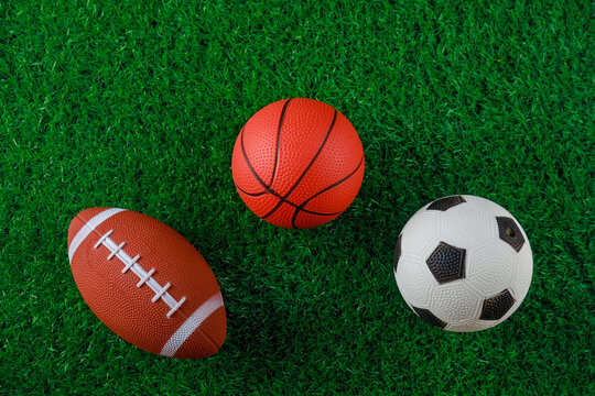 Soccer, basketball and football balls on green grass of field. © Olesya
