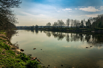 Trees, clouds and beautiful blue sky reflect on the smooth and gentle waters of the River Ribble near Preston, England.