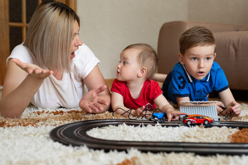 Mom and daughter and son play racing on the carpet.