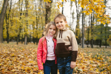 Fototapeta premium Children, a boy and a girl have fun and hug in the autumn forest among the fallen leaves