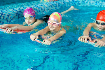 Group of boys and girls train and learn to swim in the pool with an instructor. Development of children's sports.
