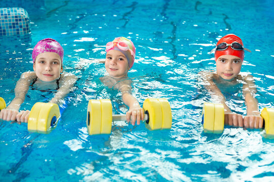 Training of children in the pool with dumbbells, swimming lessons.