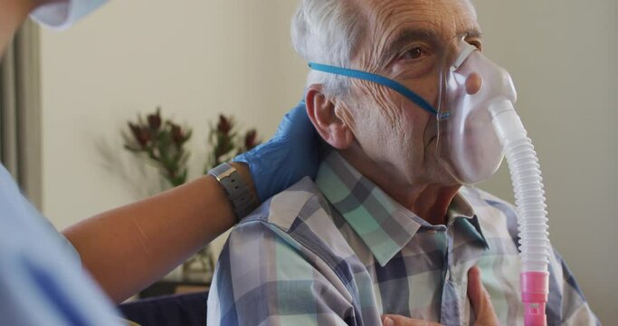 Video of biracial female doctor in face mask keeping oxygen to caucasian senior man