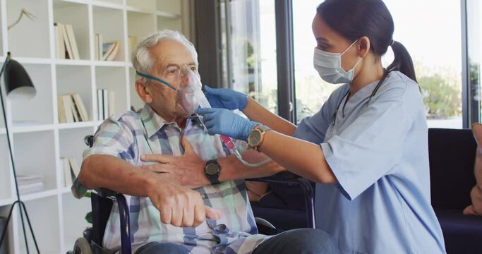 Video of biracial female doctor in face mask keeping oxygen to caucasian senior man