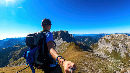 Man with backpack filming himself while hiking to the summit of Hinterer Polster in the scenic region of the Hochschwab mountain in Styria, Austria. Alpine meadows and sharp rocks. Hike concept. Free