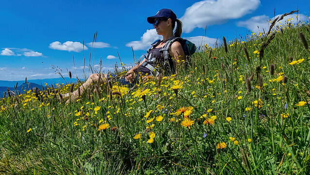 Woman resting in a field of dandelion on green grassland with panoramic view on valley in Hochschwab region in Styria, Austria. Lush green alpine spring meadows with yellow flowers. Sunny day in Alps.