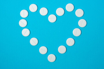 White pills on a blue background. The pills is laid out in the shape of a heart. Prevention and treatment of heart and cardiovascular diseases. Vitamin tablets