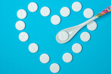 White pills on a blue background. The pills is laid out in the shape of a heart. Prevention and treatment of heart and cardiovascular diseases. Vitamin tablets