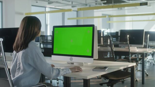Asian Business Woman Working on Desktop Computer with Green Screen Mock Up Display in Busy Creative Office. Beautiful Diverse Female Manager Surfing Internet in Green Screen Notebook.