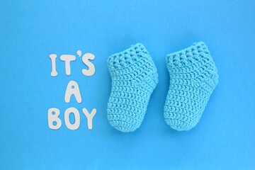 It's a boy lettering, crochet baby booties on blue background. Baby boy birth, new life, family concept. Greeting card idea for newborn. Pregnancy announcement. Flatlay, top view