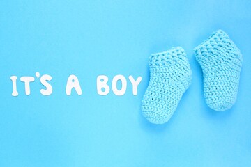 It's a boy lettering, crochet baby booties on blue background. Baby boy birth, new life, family concept. Greeting card idea for newborn. Pregnancy announcement. Flatlay, top view