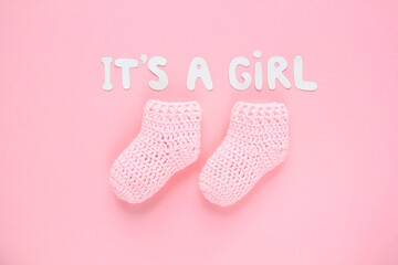 It's a girl lettering, crochet baby booties on pink background. Baby girl birth, new life, family concept. Greeting card idea for newborn. Pregnancy announcement. Flatlay, top view